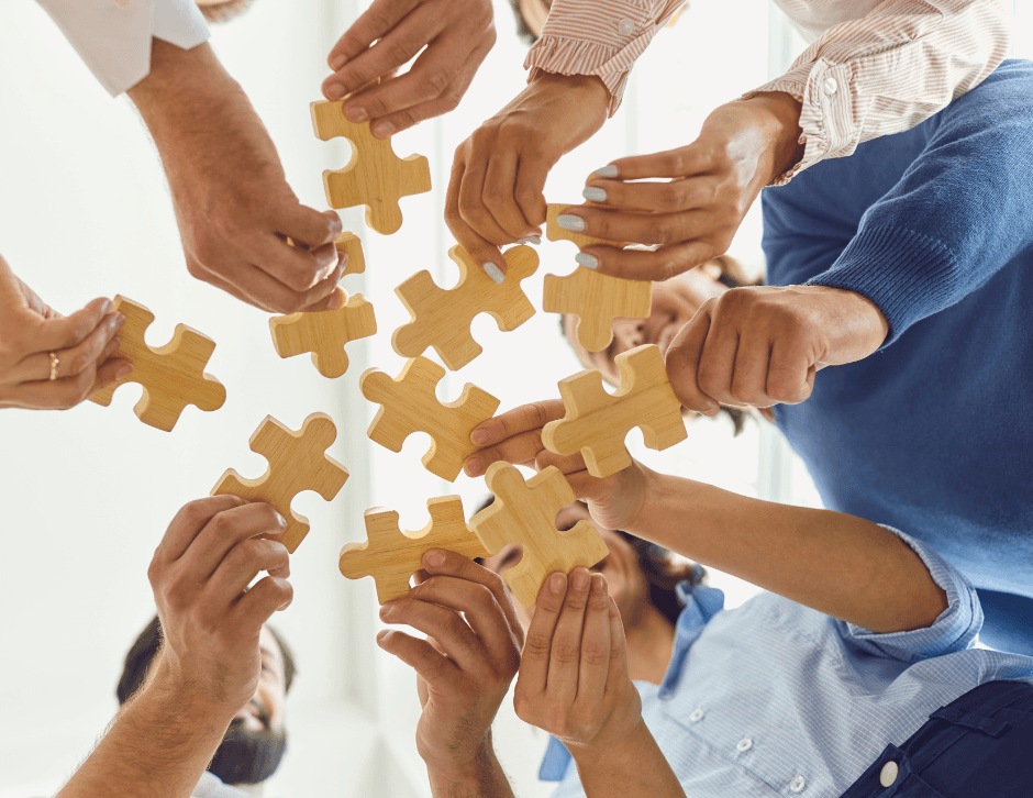 Multiple hands working together to assemble puzzle pieces, representing collaboration, partnership and shared problem-solving.